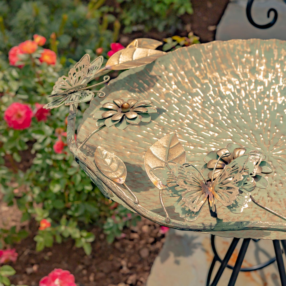 Close-up of a gold-toned birdbath bowl decorated with metal butterflies, flowers, and leaves.