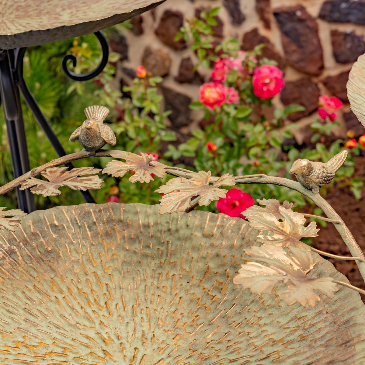 Close-up of a textured birdbath rim decorated with gold-tone leaves and two perched birds.