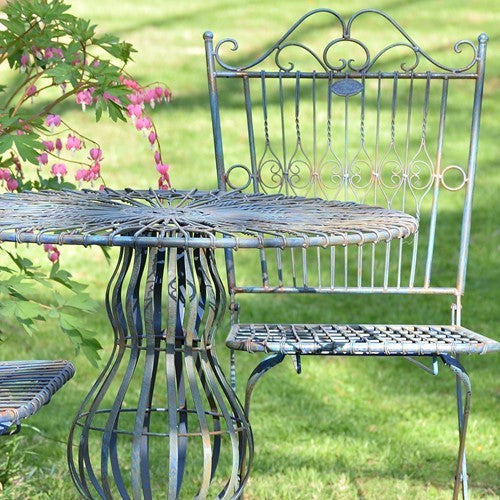 Close view of an ornate metal bistro table and chair among garden flowers.