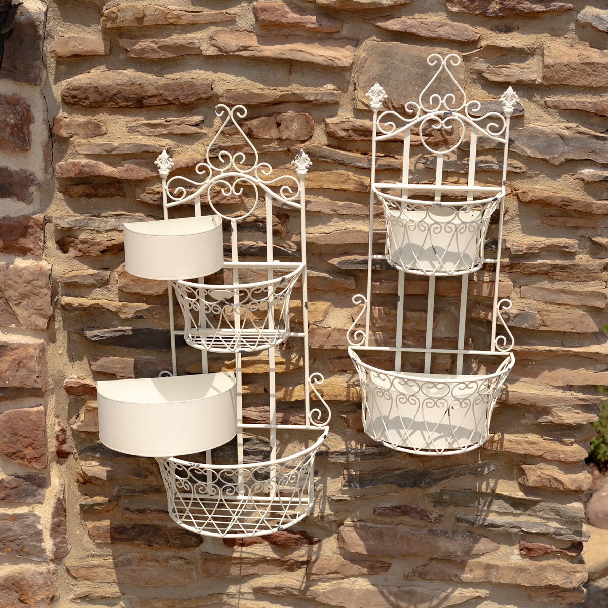 Two ornate white wall planters mounted on a stone wall, with pale inserts in some baskets.