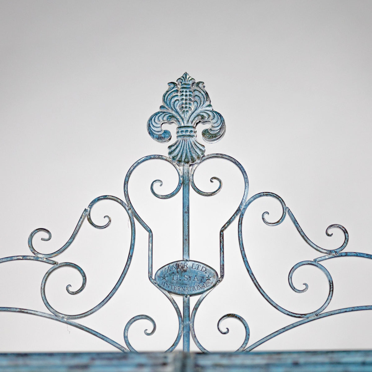 Close-up of an ornate blue-gray iron panel with symmetrical scrolls and a fleur-de-lis crest.