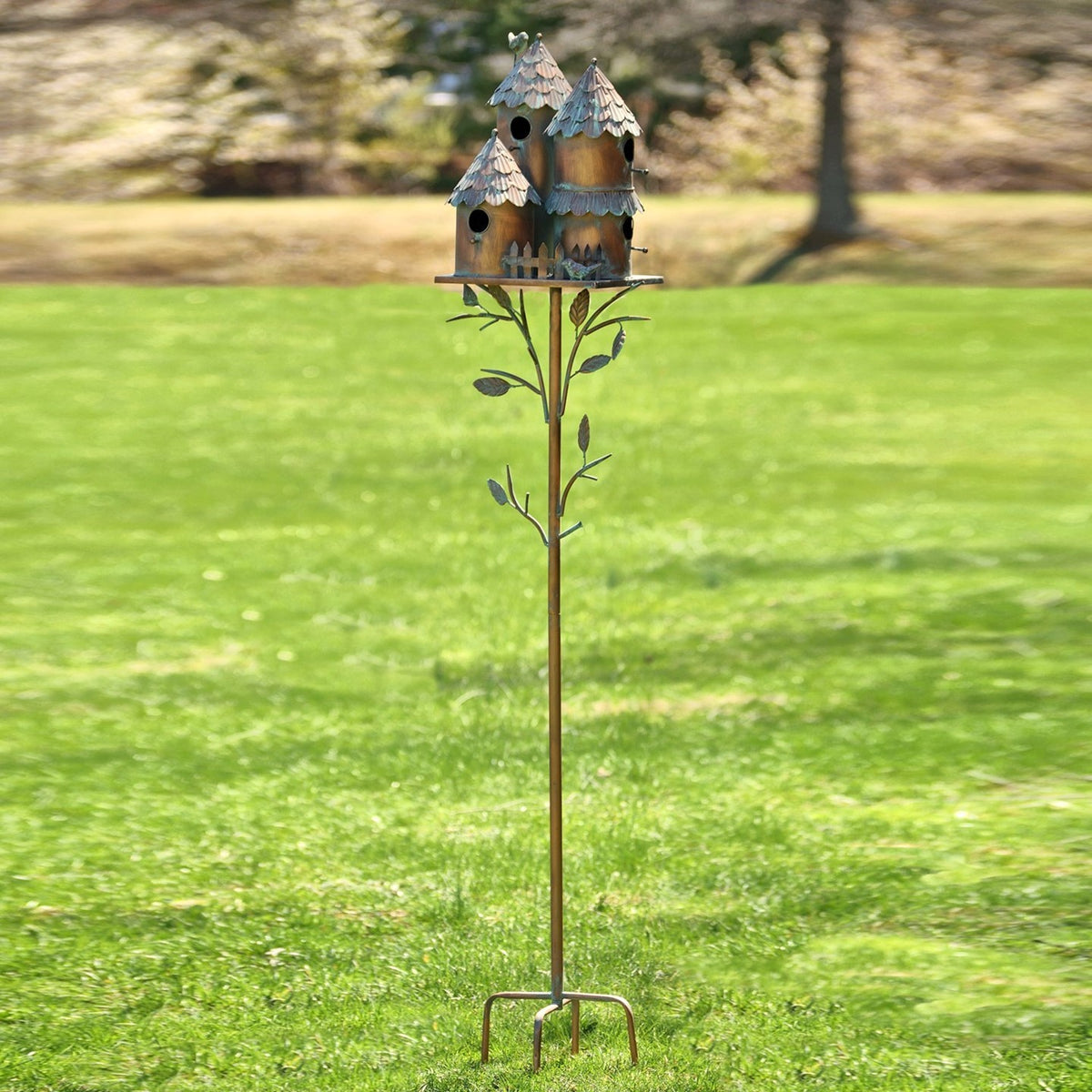 Tall metal garden stake topped with clustered birdhouses, standing in a green lawn.