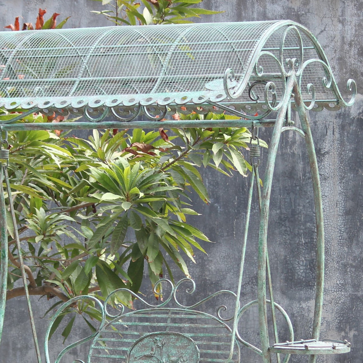 Close view of the swing bench’s curved metal canopy, scrollwork trim, and supporting frame against garden foliage.