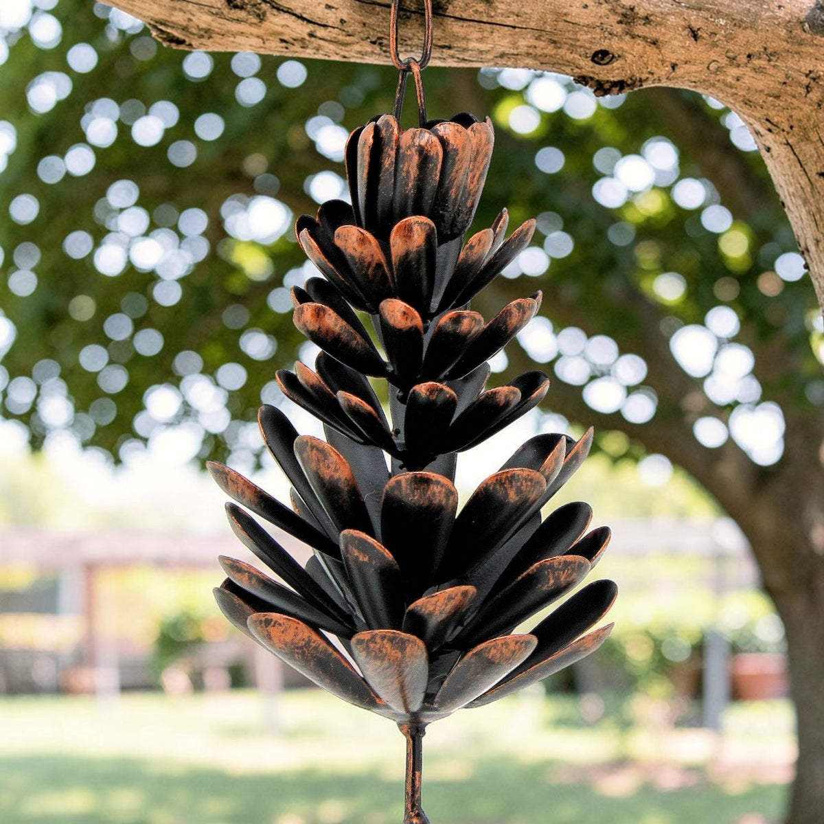 Close-up of a dark metal pinecone-shaped pendant hanging from a wooden branch.