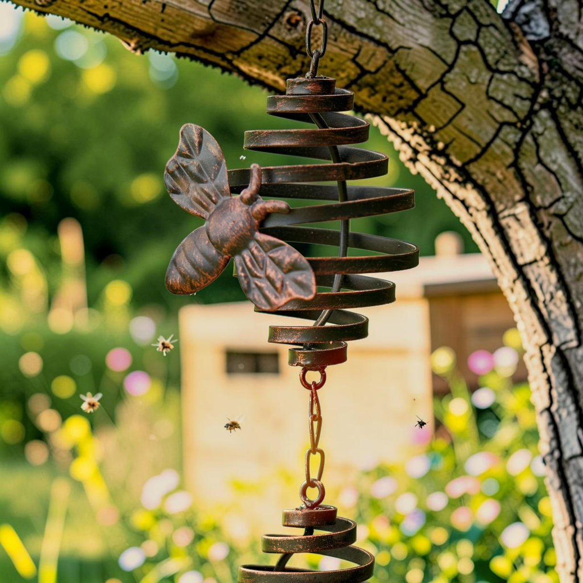 Antique bronze spiral rain chain with a honeybee ornament hanging from a tree branch.