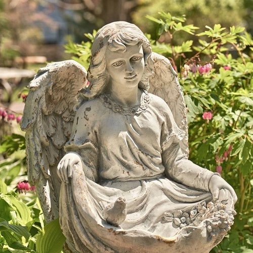 Antique-gray angel child statue seated outdoors, with birds gathered on the folds of its robe.