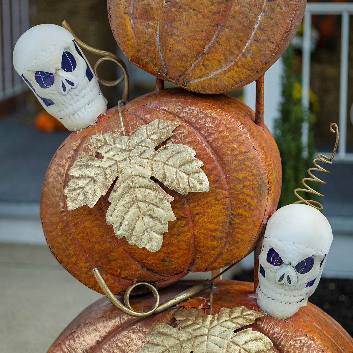 Close-up of textured orange pumpkins, pale leaves, curled metal accents, and white skulls with purple eyes.