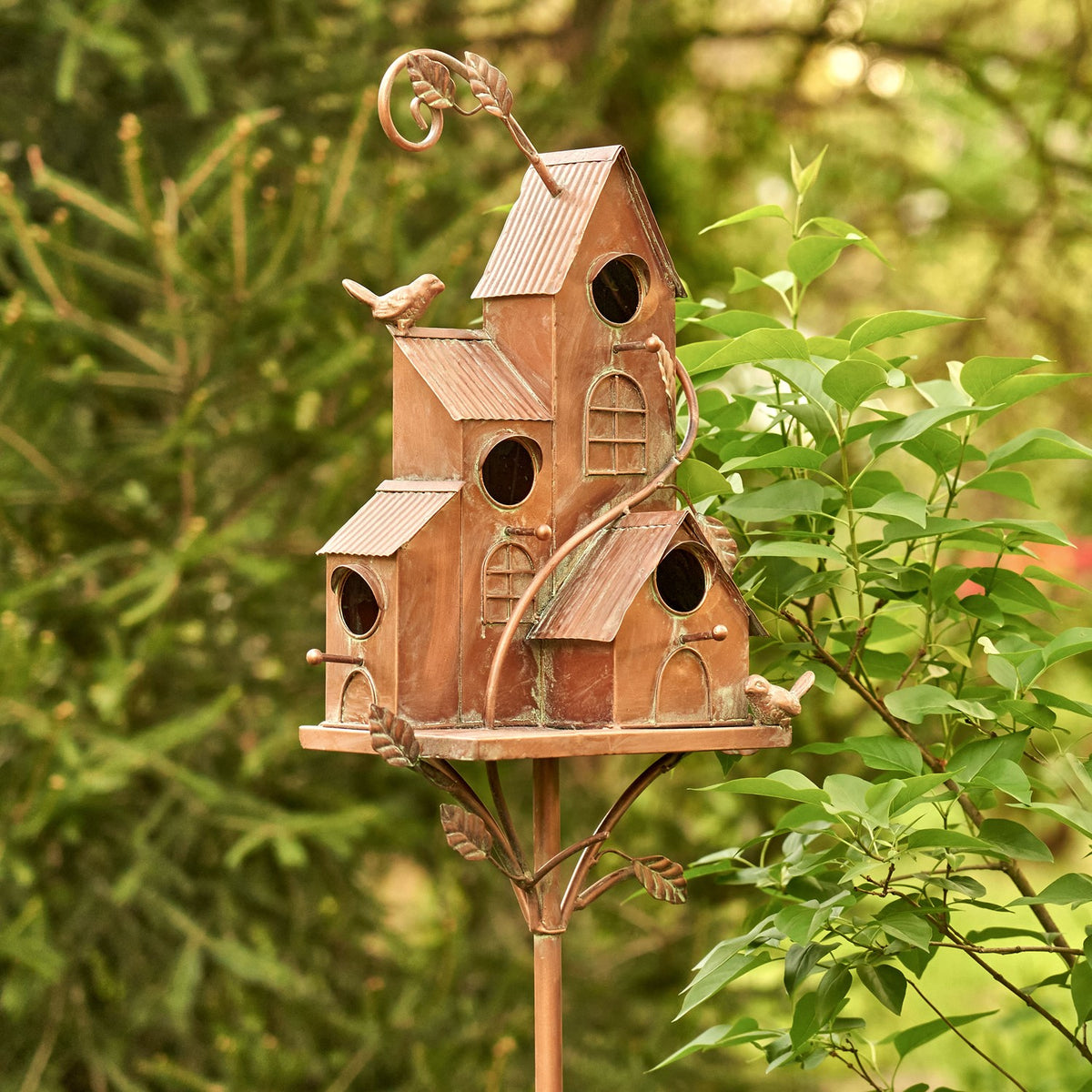 Full birdhouse stake with copper finish viewed at an angle among garden plants