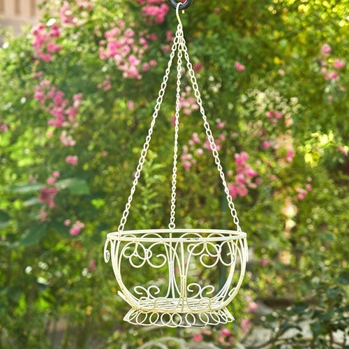 Cream ornamental wire basket hanging by three chains against a garden backdrop