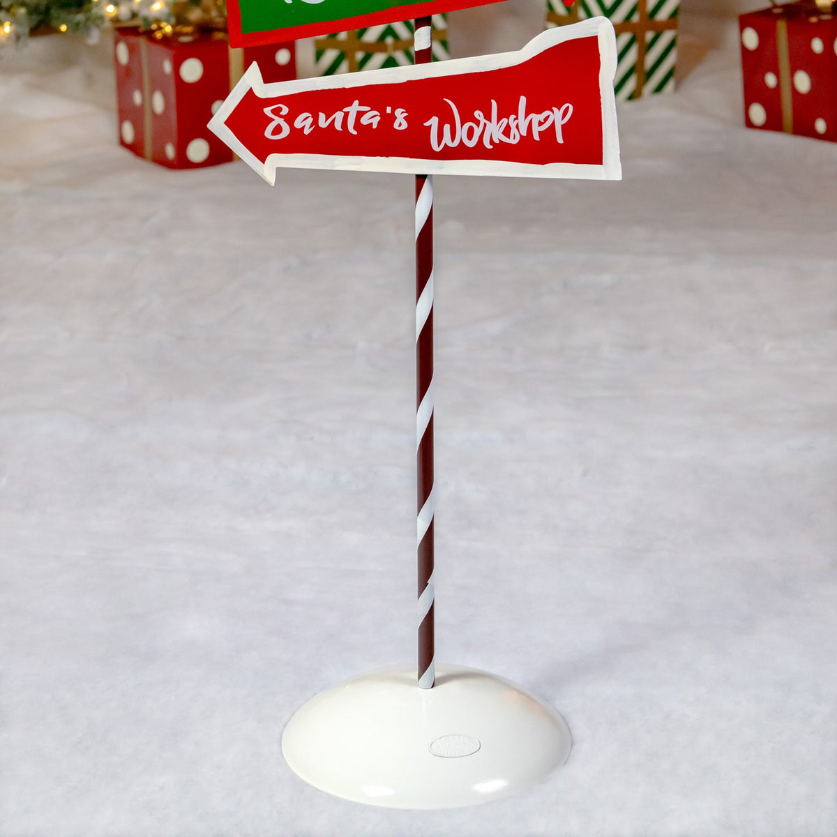 Close view of a striped pole, round base, and red directional sign on a snowy holiday set.