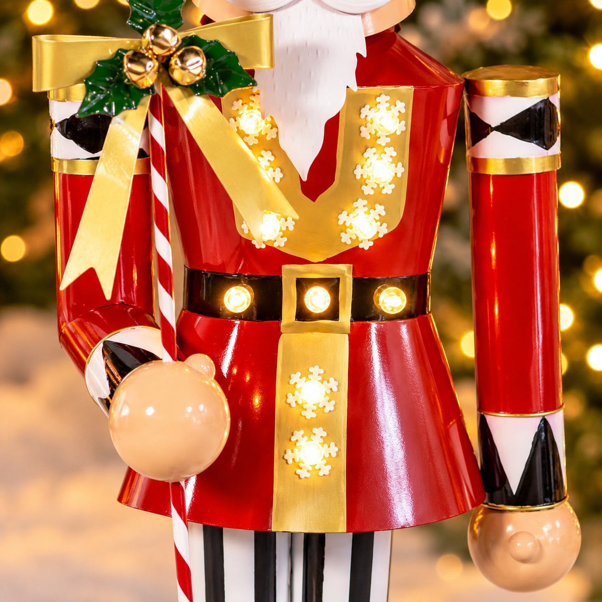 Close view of the nutcracker’s red and gold uniform, glowing lights, candy cane staff, and hand.