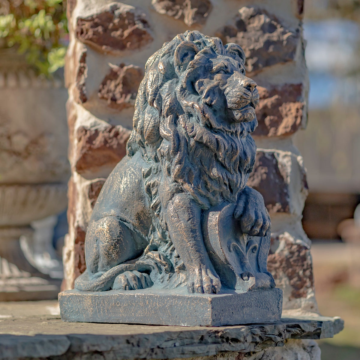 Close view of a seated guardian lion statue on a stone ledge, with a textured mane and one paw resting on a shield.