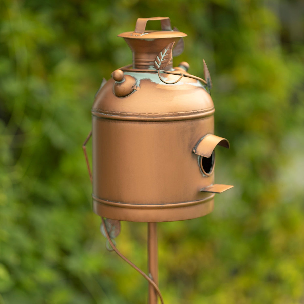 Antique copper milk-can birdhouse on a garden stake, shown at an angle with its side entrance and leaf accents.