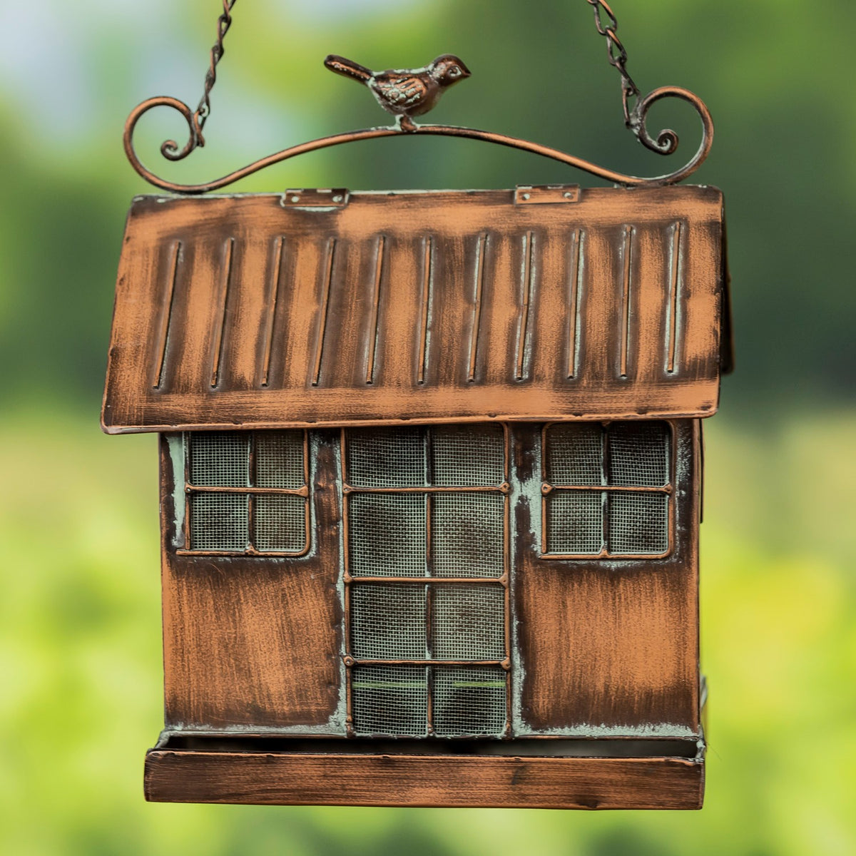 Front of a copper-toned hanging bird feeder with a pitched roof, mesh windows, curled hanging frame, and bird ornament.