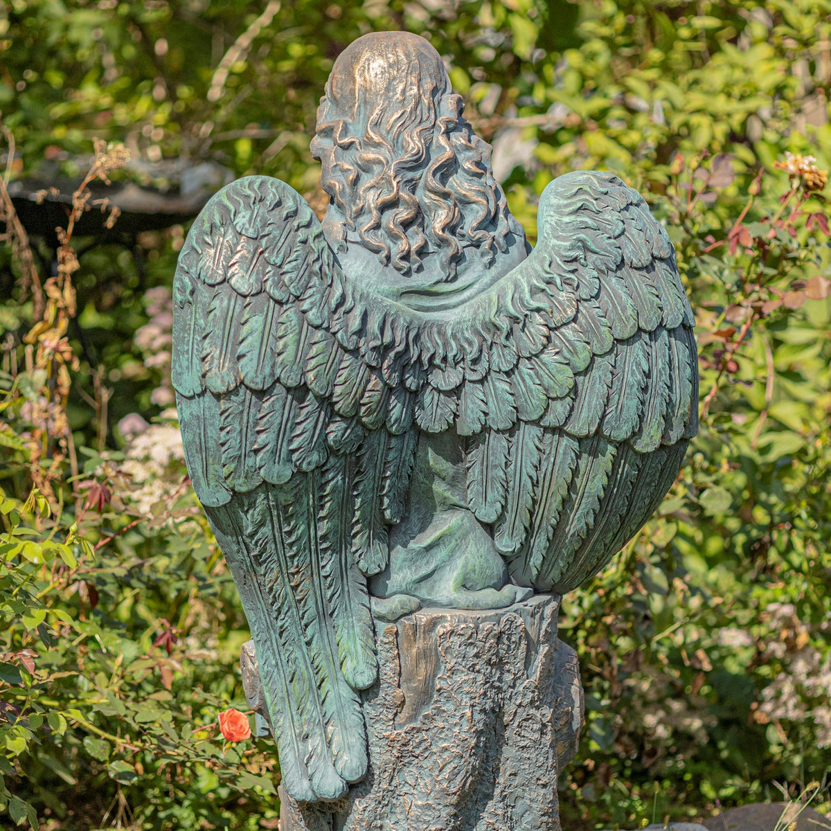 Rear view of the seated angel statue, showing long wavy hair, broad feathered wings, and a textured base.