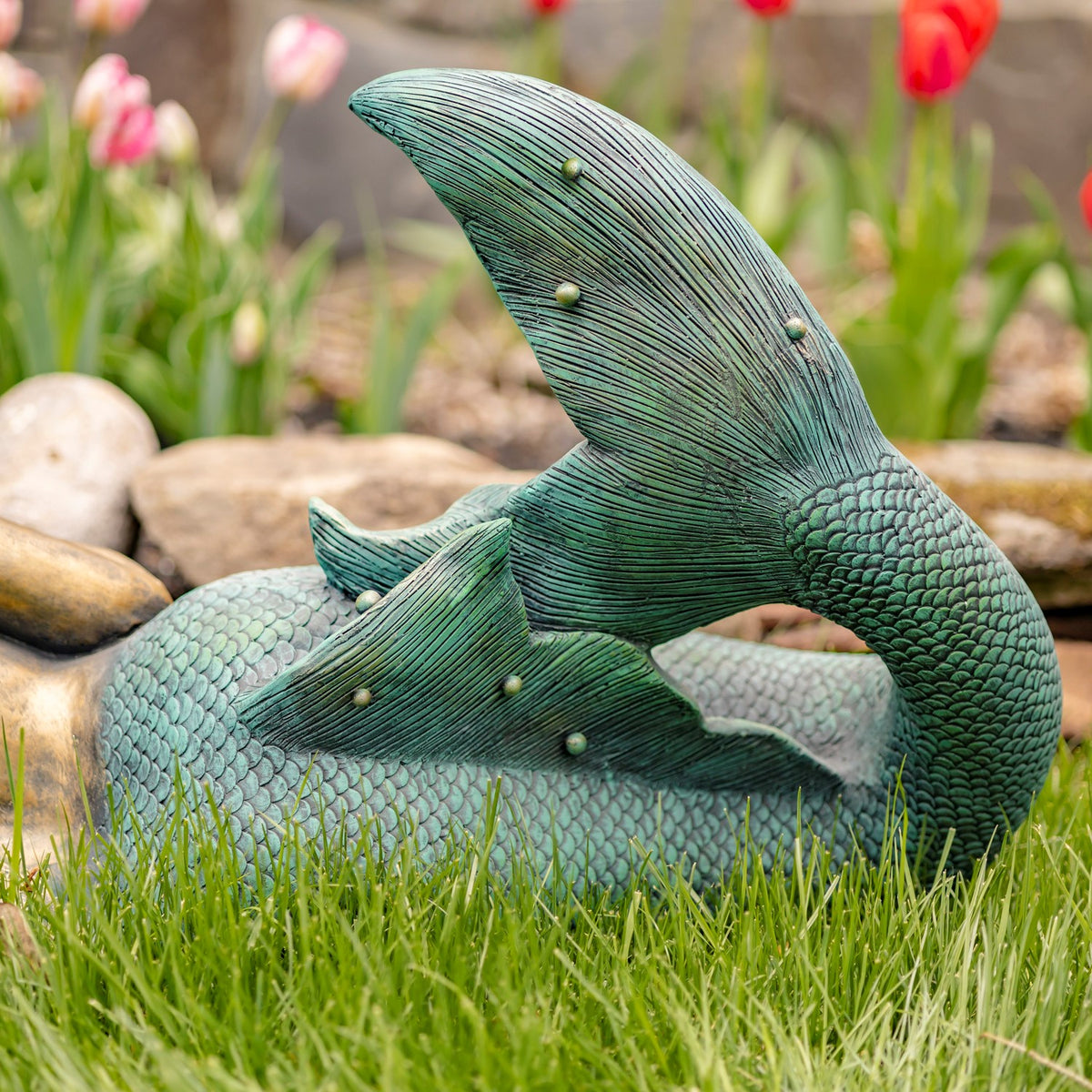 Close view of the mermaid statue’s textured teal tail curled above the grass.
