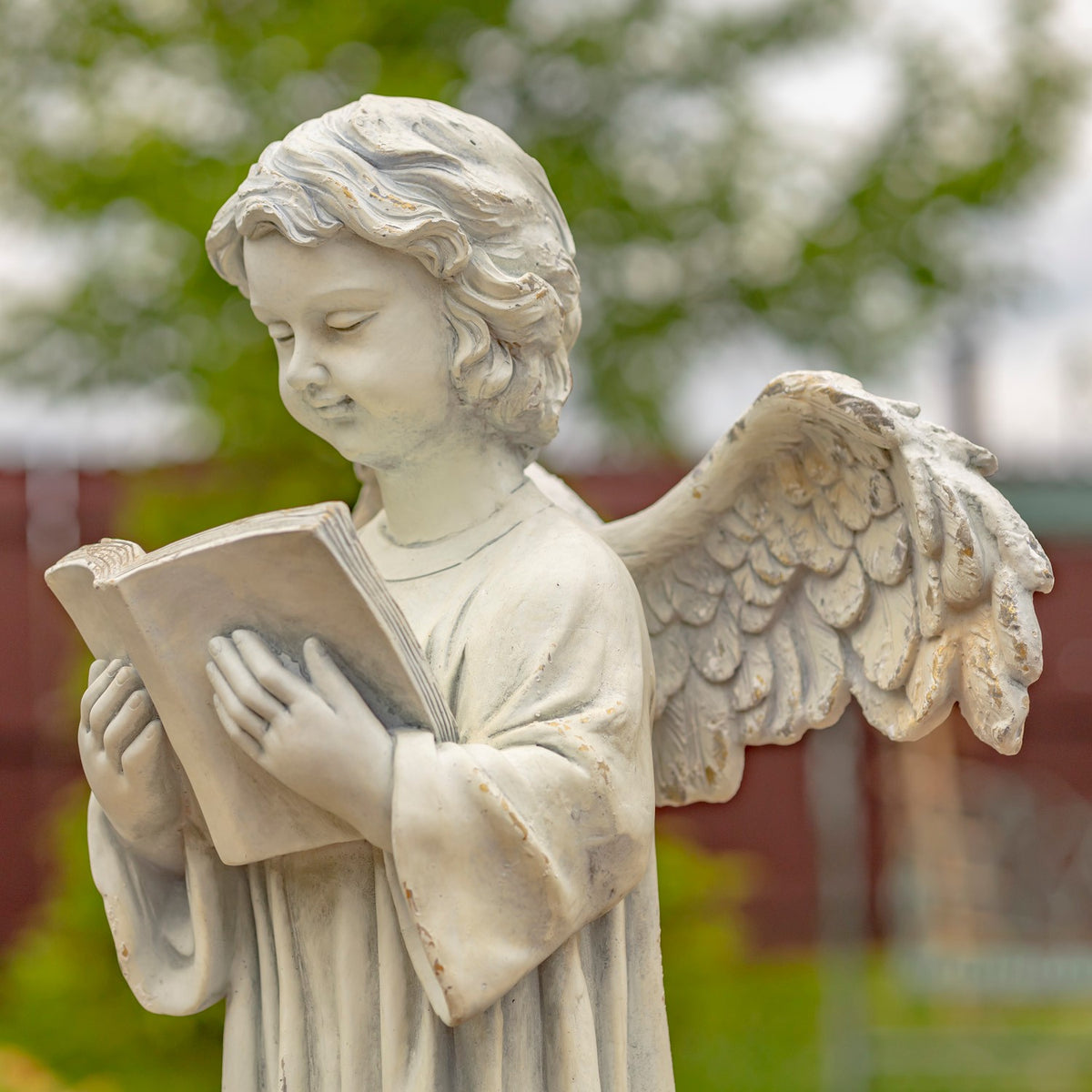 The angel looks down at an open book, with carved hair, hands and one detailed wing in view.