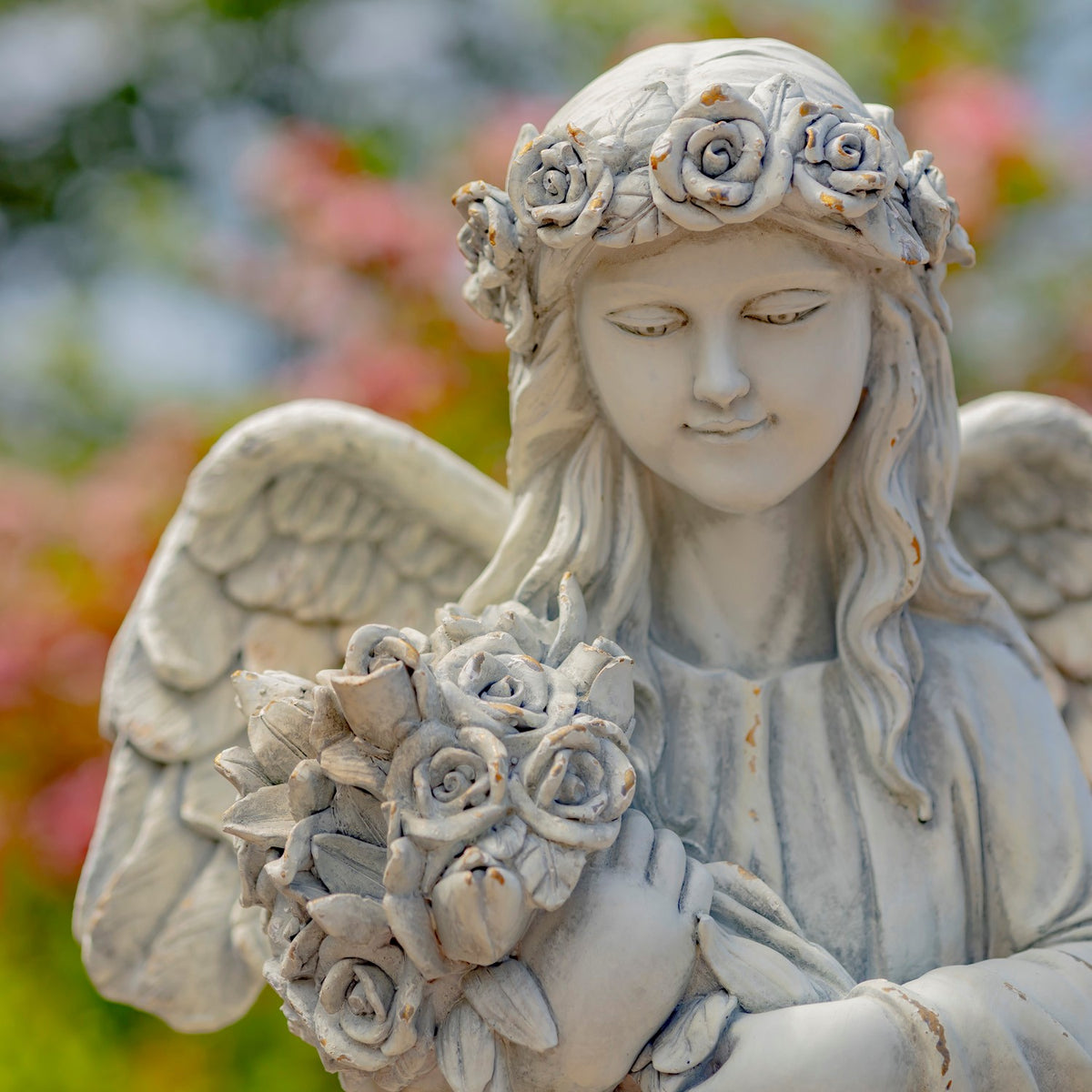 Close view of the angel’s rose crown, face, wing, and bouquet of sculpted flowers.