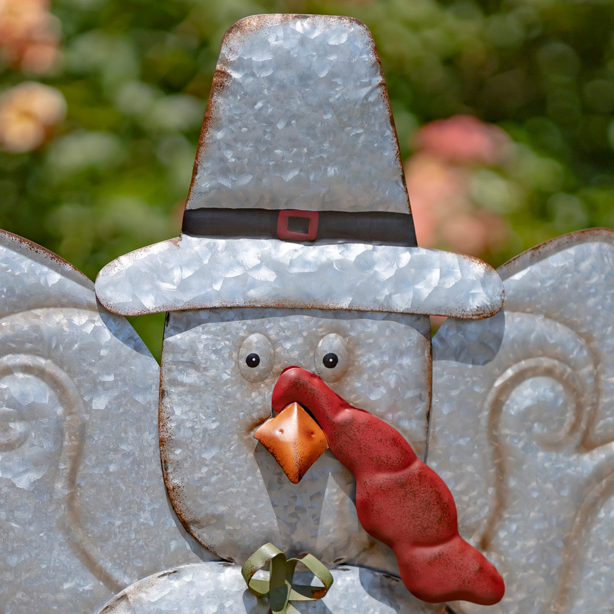 Galvanized turkey face with a black hat, red wattle, orange beak, and small bow tie.