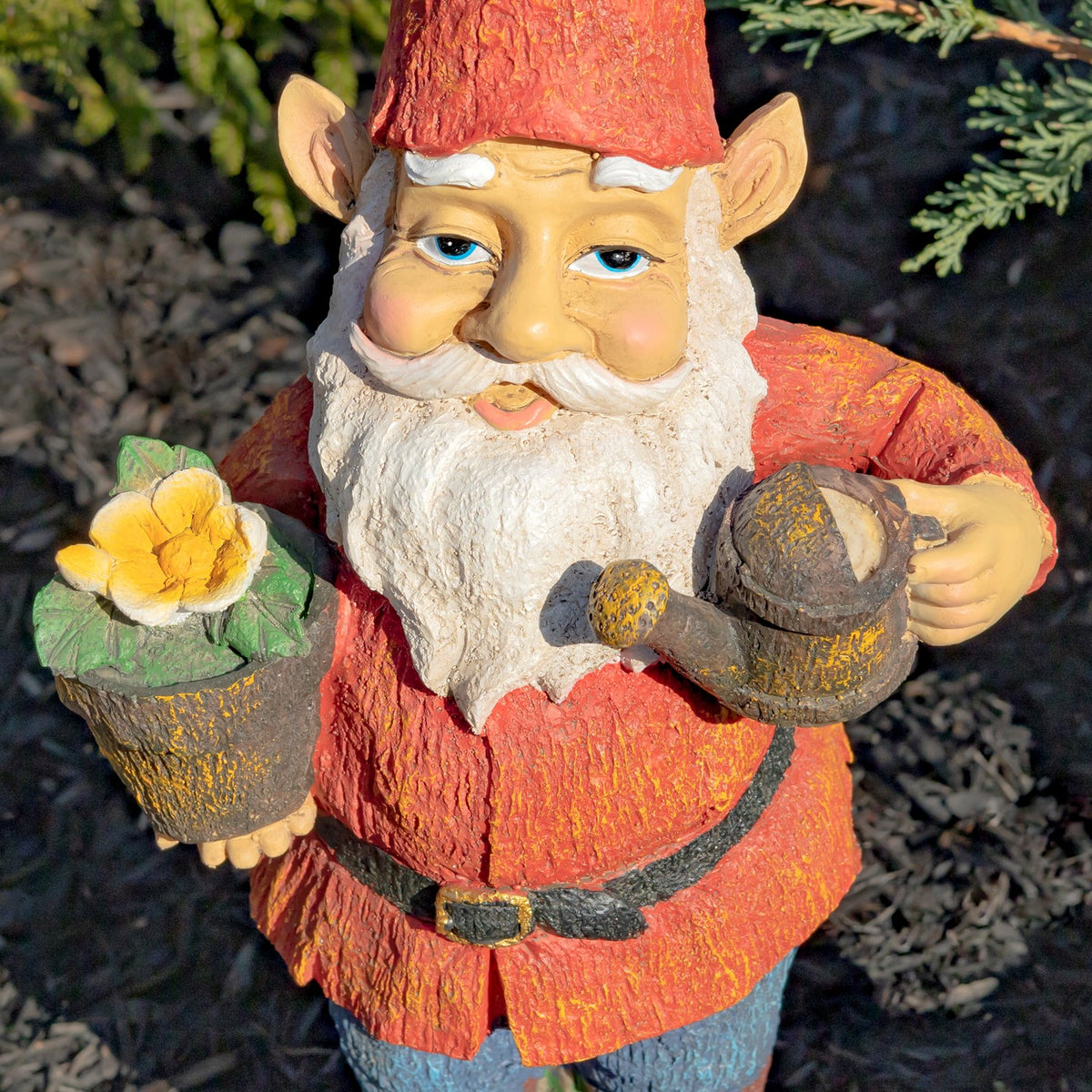 Close view of a red-hatted garden gnome holding a flower pot with a yellow bloom and a small watering can.