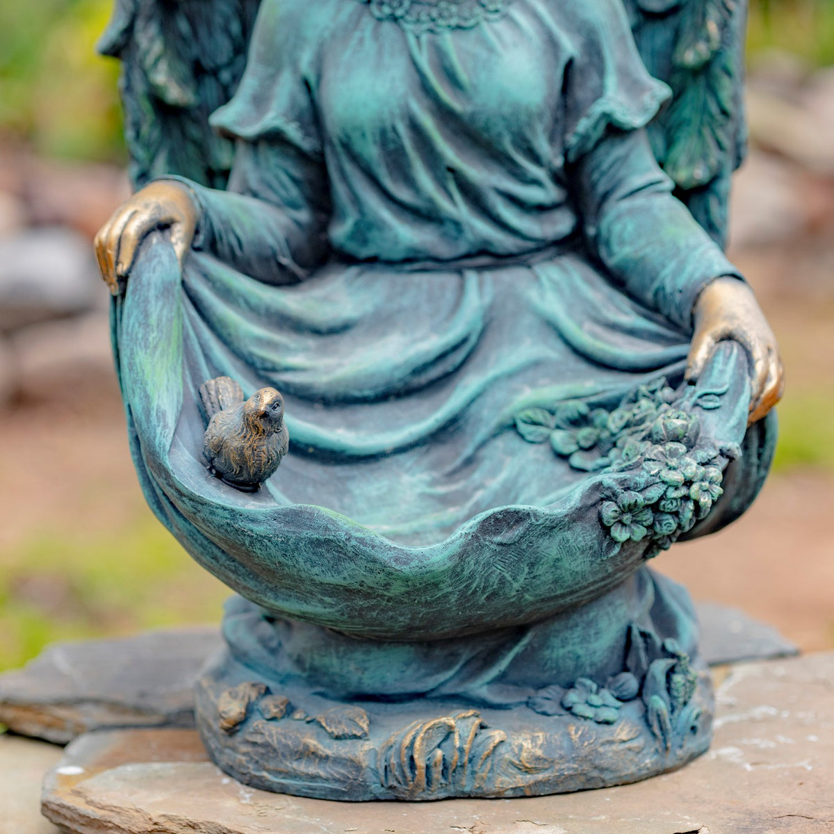 Close-up of the kneeling angel statue’s hands, birdbath bowl, small bird, and floral relief.