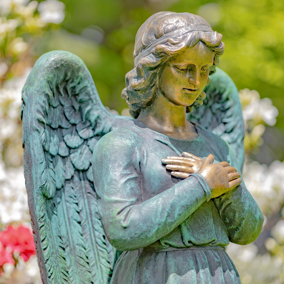 Close view of an angel statue with hands clasped over a small heart, showing a weathered blue-green finish.