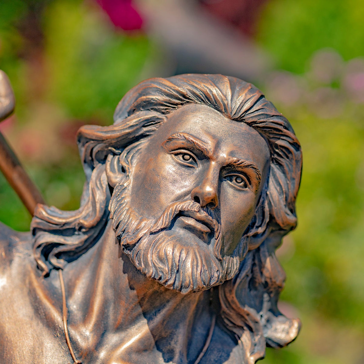 Close-up of the bearded merman statue’s face, with swept-back hair and a weathered bronze finish.