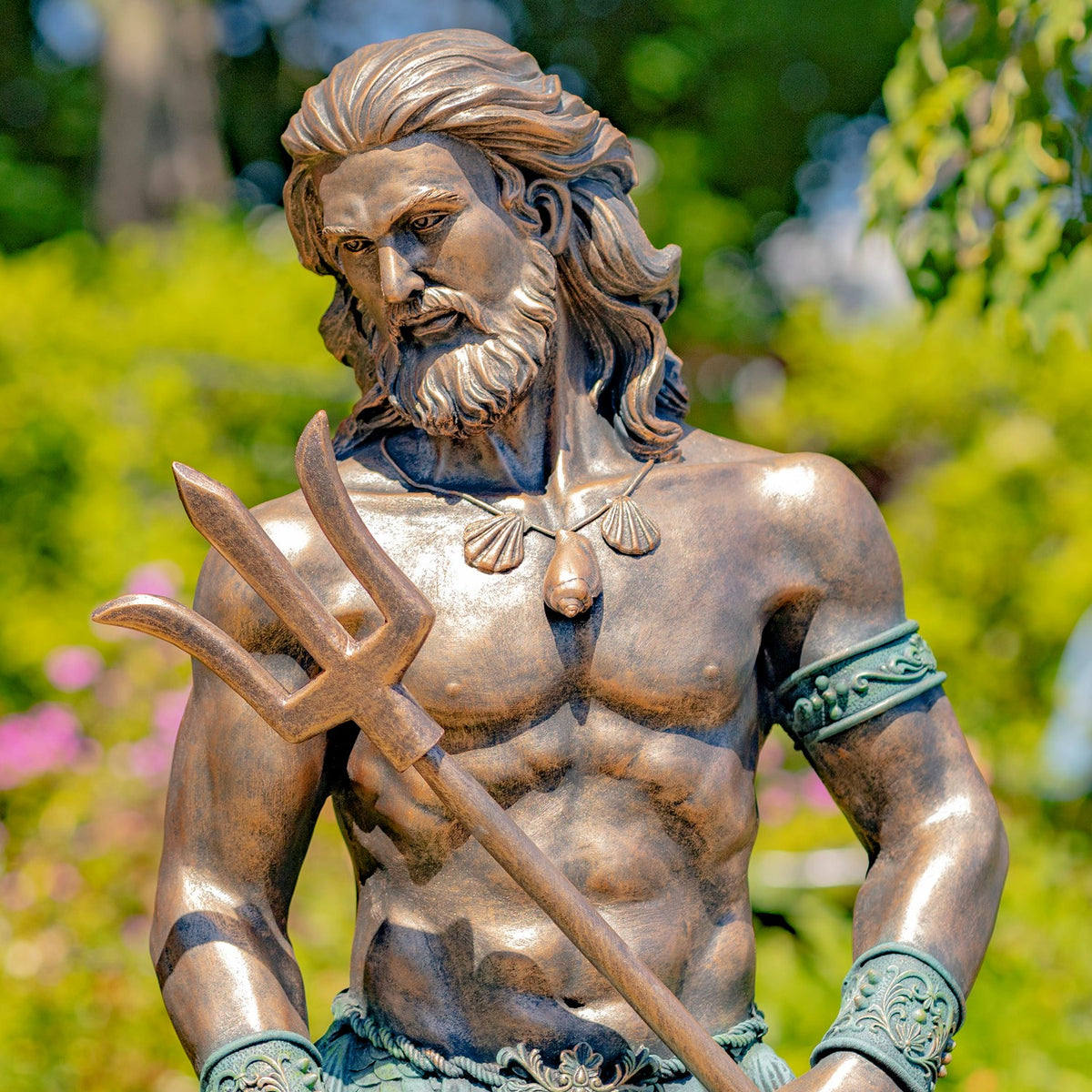 Bronze-toned merman statue holding a trident outdoors, shown from the waist up against greenery.