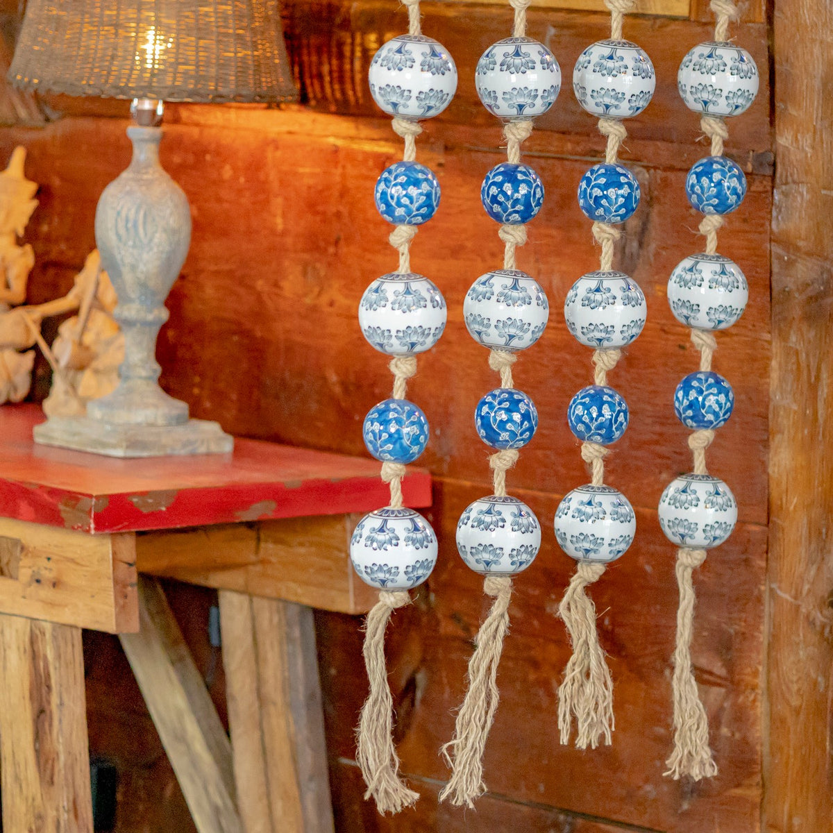 Blue-and-white patterned ceramic balls hang in rows on knotted natural rope beside a rustic wooden table.