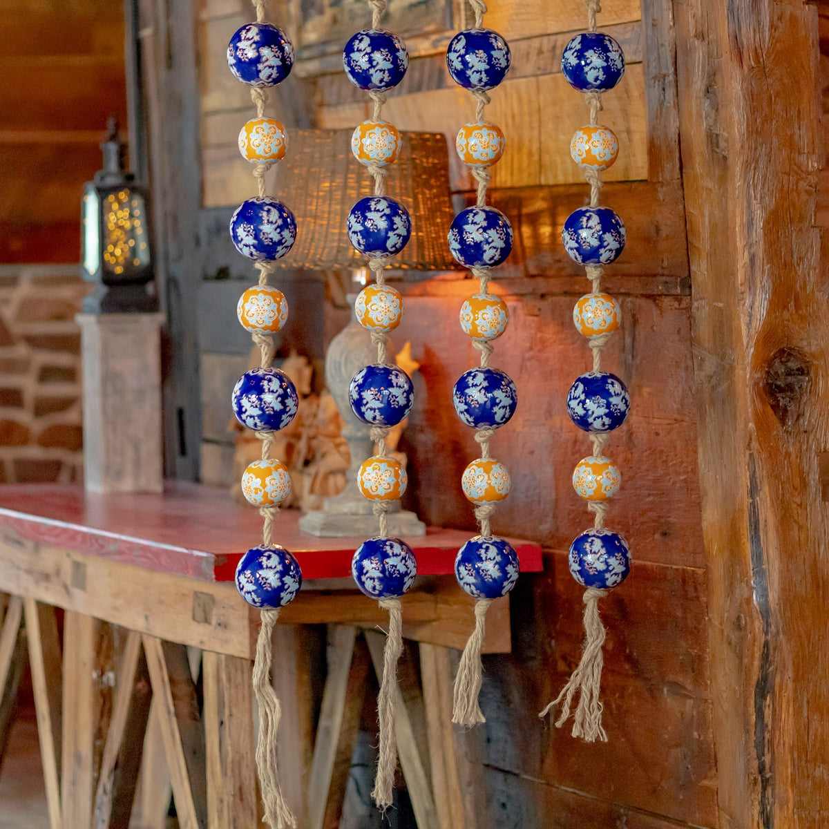 Blue and orange patterned ceramic balls hang in four strands against a rustic wooden backdrop.