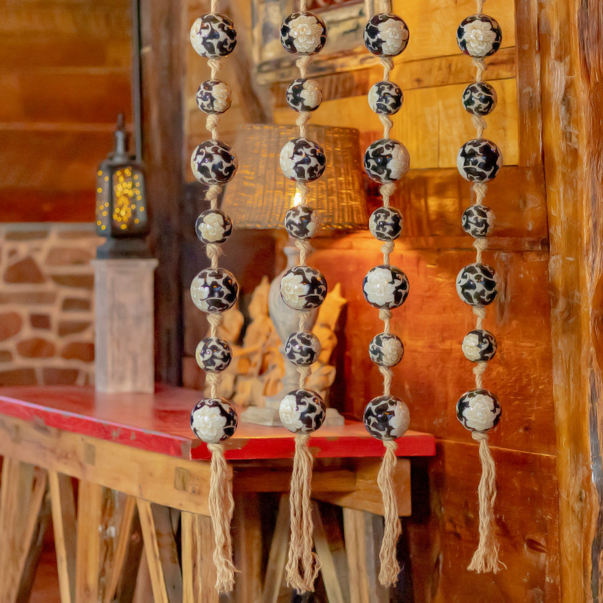 Four strands of black-and-white patterned ceramic balls hang in a warmly lit wooden room.