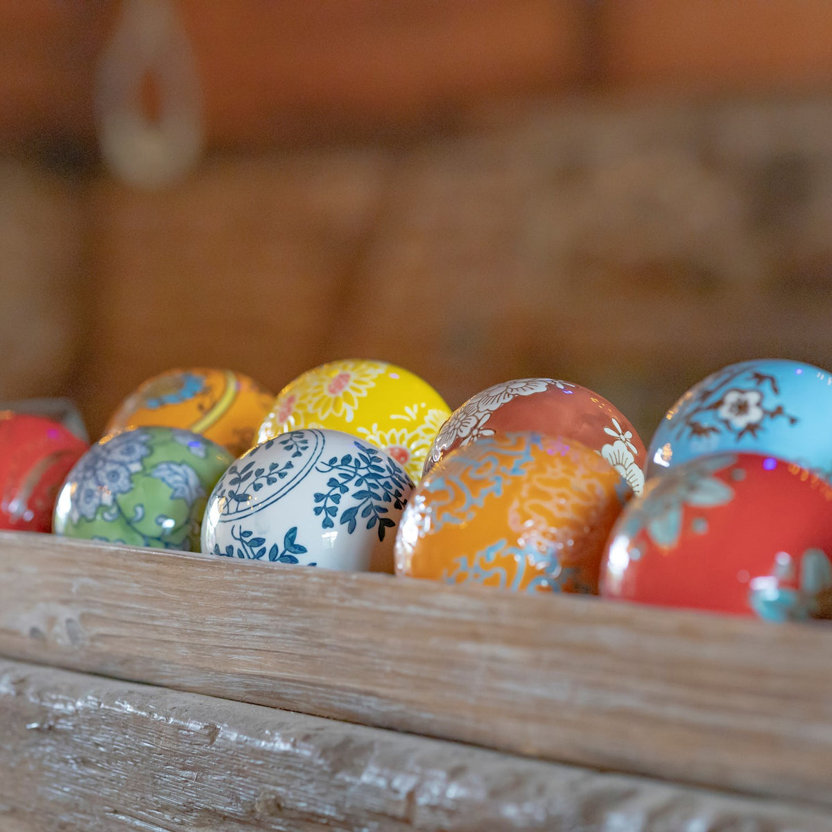 Patterned ceramic balls in bright colors sit in a weathered wooden tray.