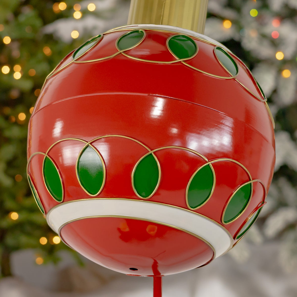 Close-up of a glossy red Christmas ball ornament with green and gold trim against a blurred evergreen background.