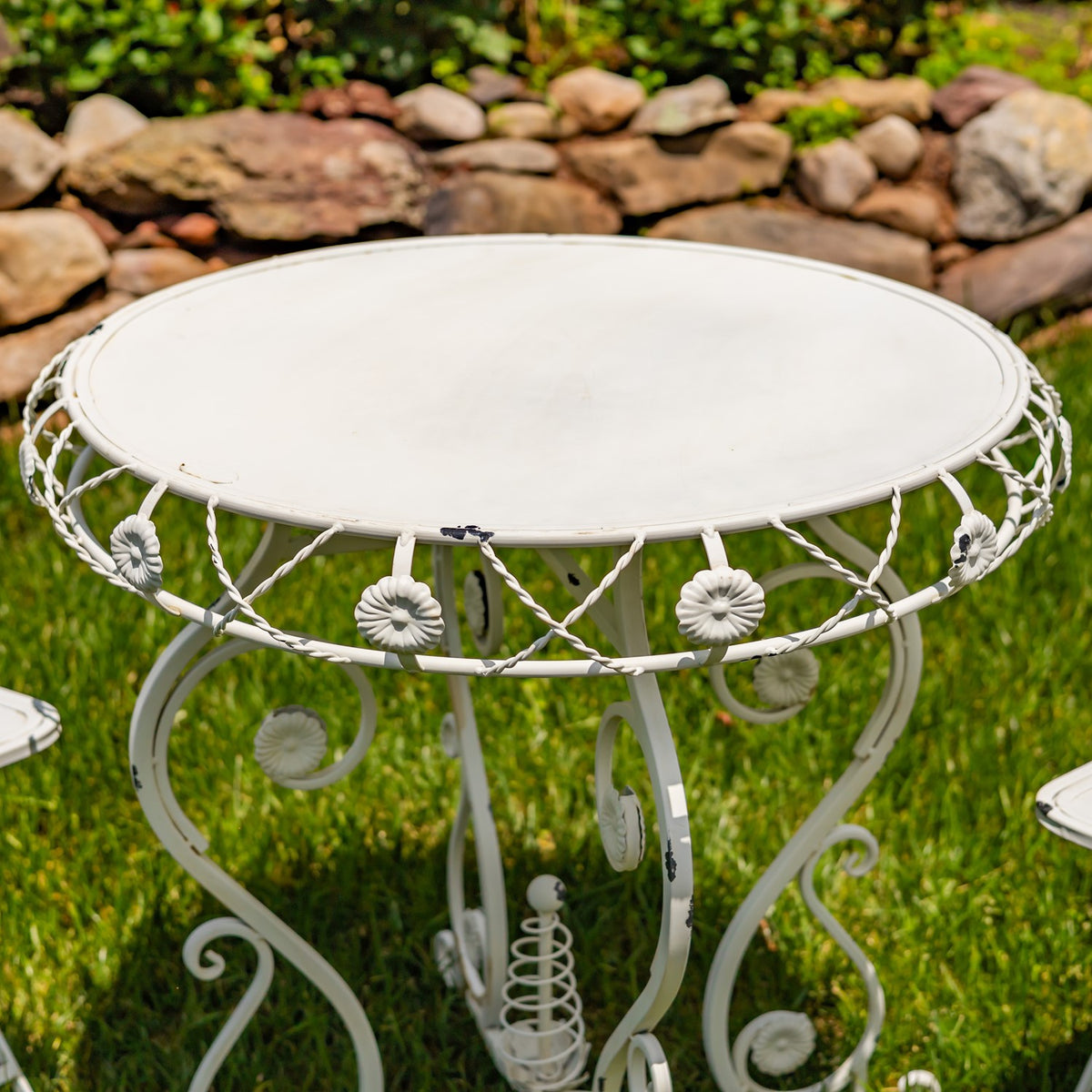 Close view of a pale round metal tabletop with flower accents around its curled frame.