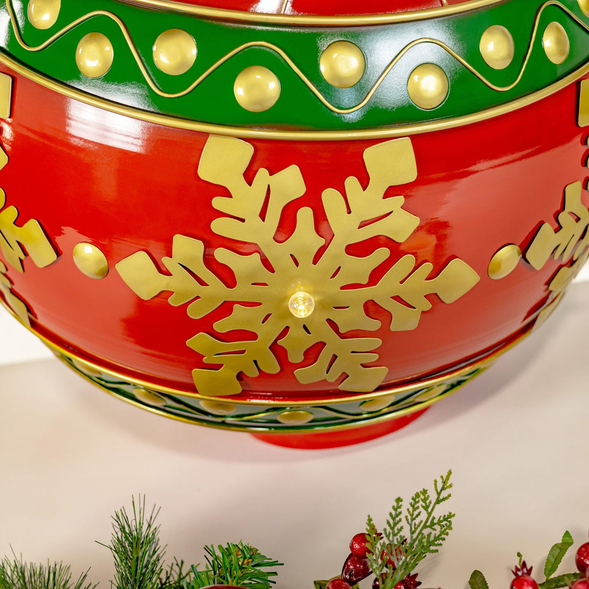 Close-up of a red and green metal ornament with gold snowflake cutouts and glowing lights.