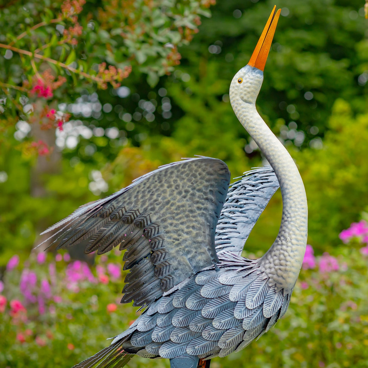 Side view of a blue-grey heron figurine with one wing spread in a garden