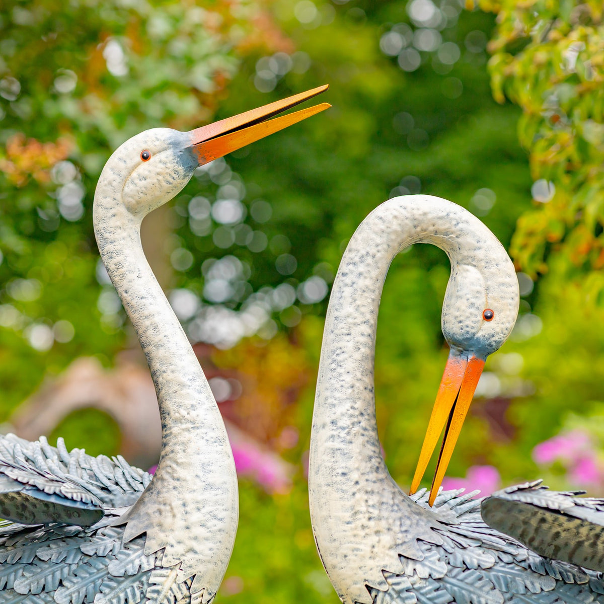 Close view of two egret figurines' heads and upper bodies outdoors