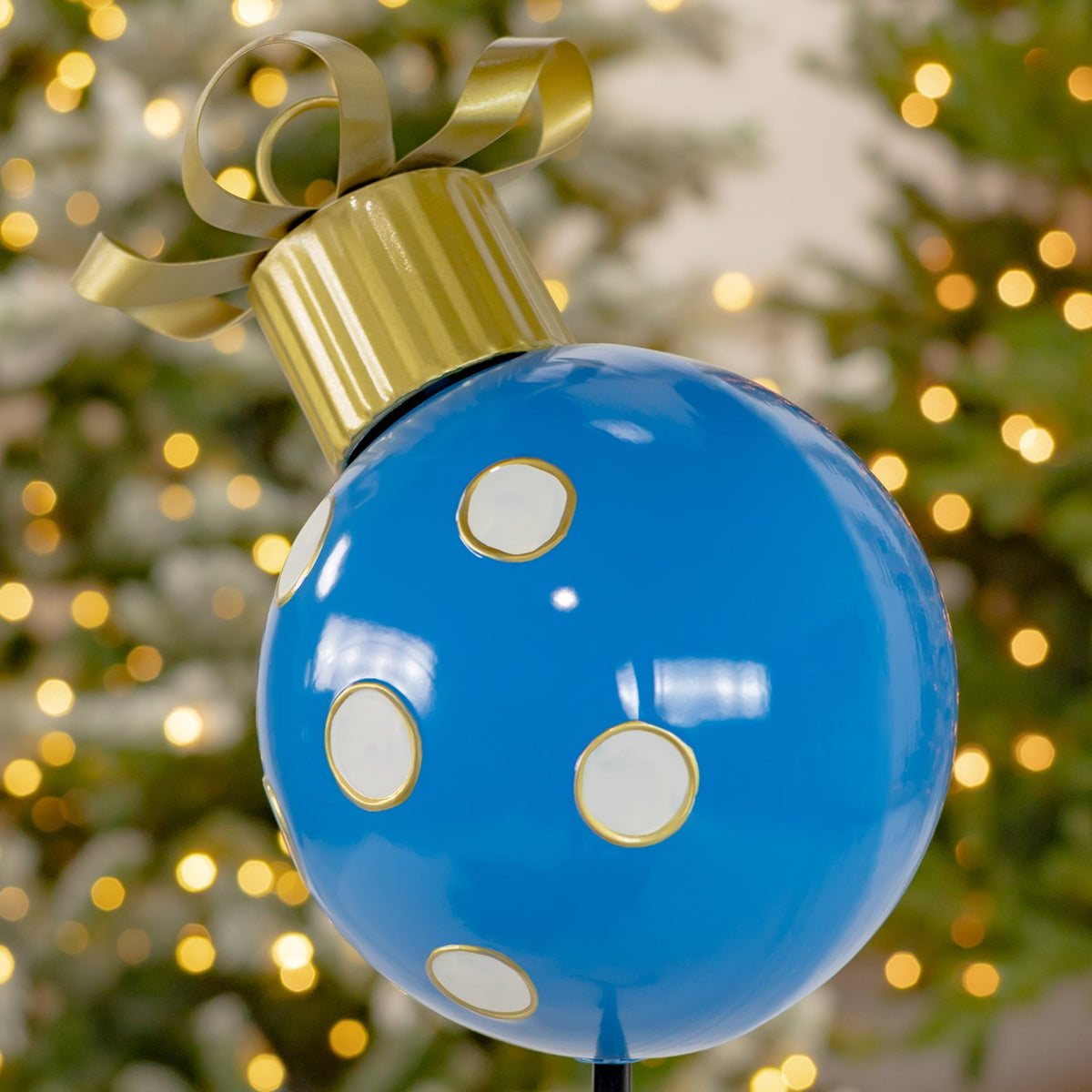 Close-up of a glossy blue ball ornament with white, gold-edged dots and a gold ribbon bow.