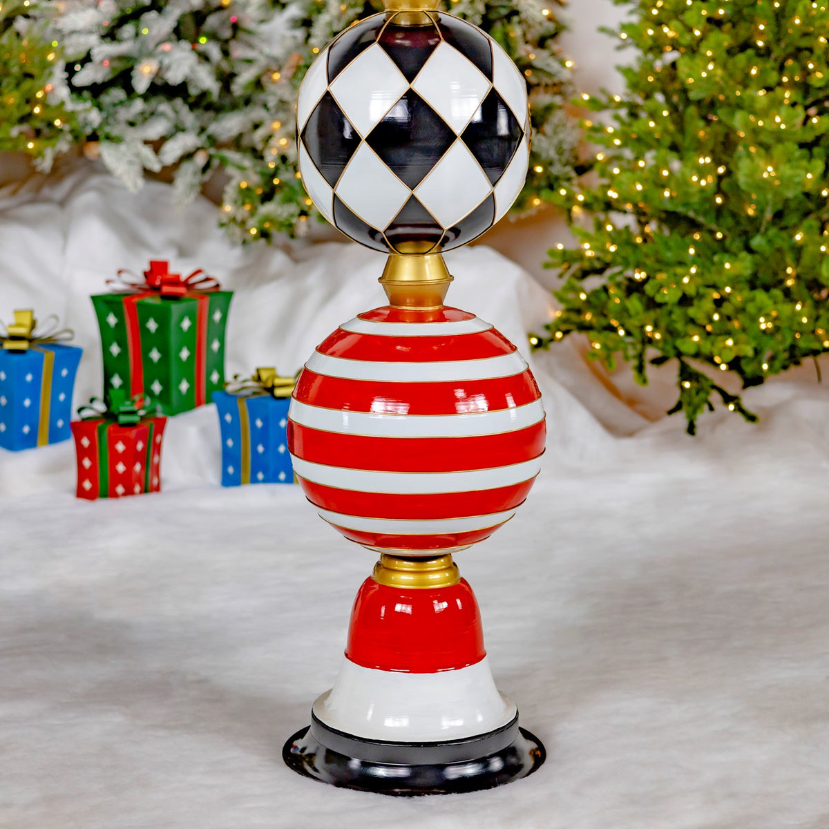 A red-and-white striped ornament tower with a black-and-white patterned top stands beneath a lit Christmas tree.