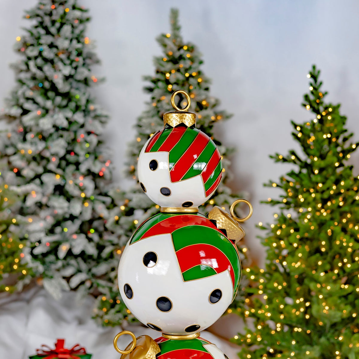 Close view of stacked red, green, and white ornament spheres with black dots among lit Christmas trees.