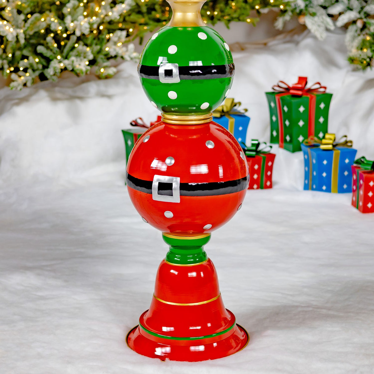 A glossy red and green ornament tower with black belt bands and silver buckles stands among Christmas gifts.