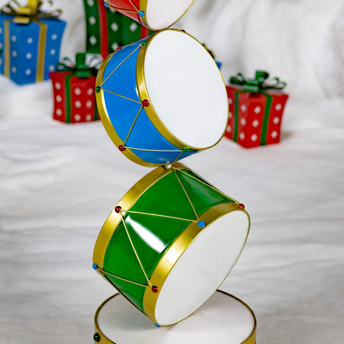 Close view of a colorful stacked drum display tower with gold trim, set among wrapped presents.