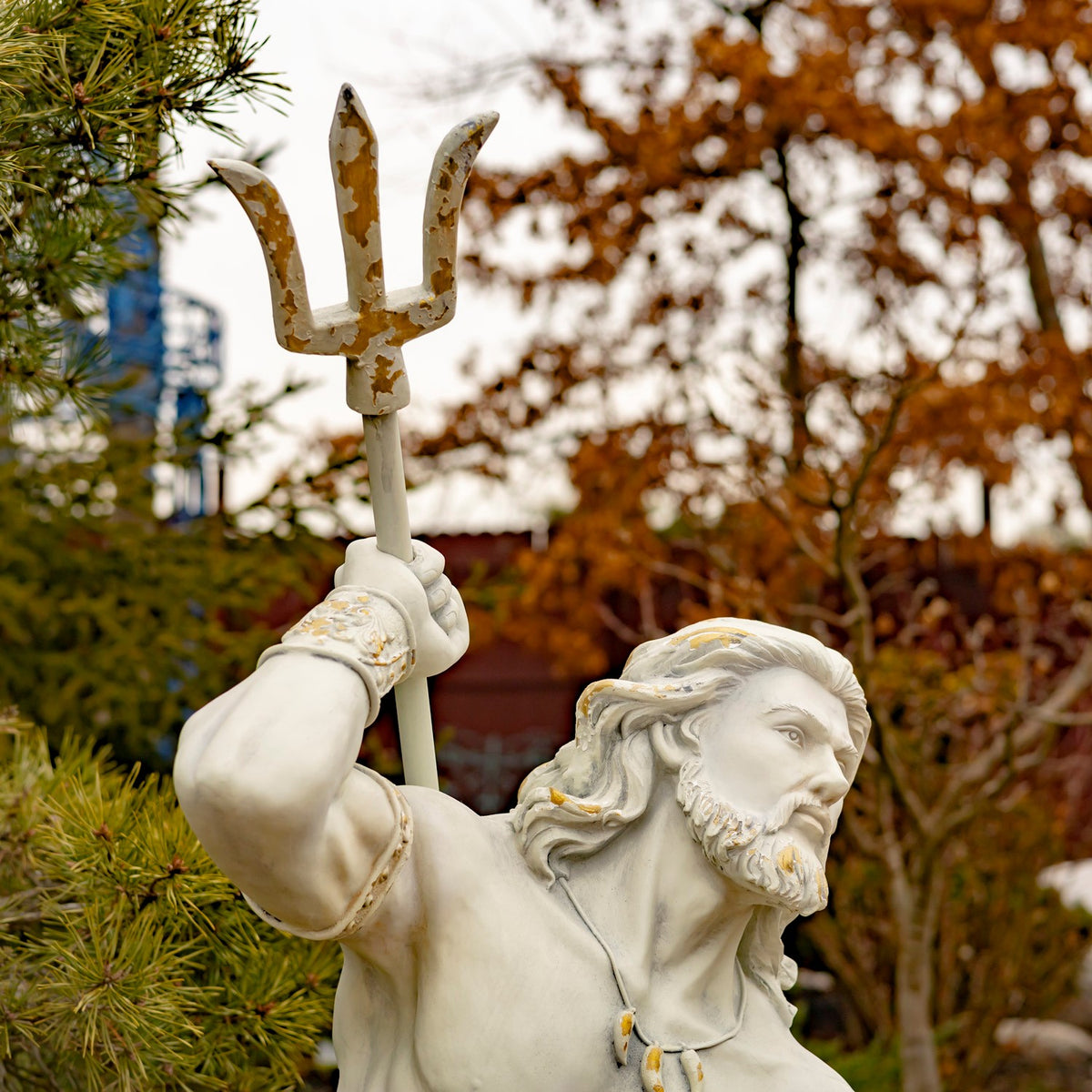A bearded merman statue raises a three-pronged trident among garden trees.