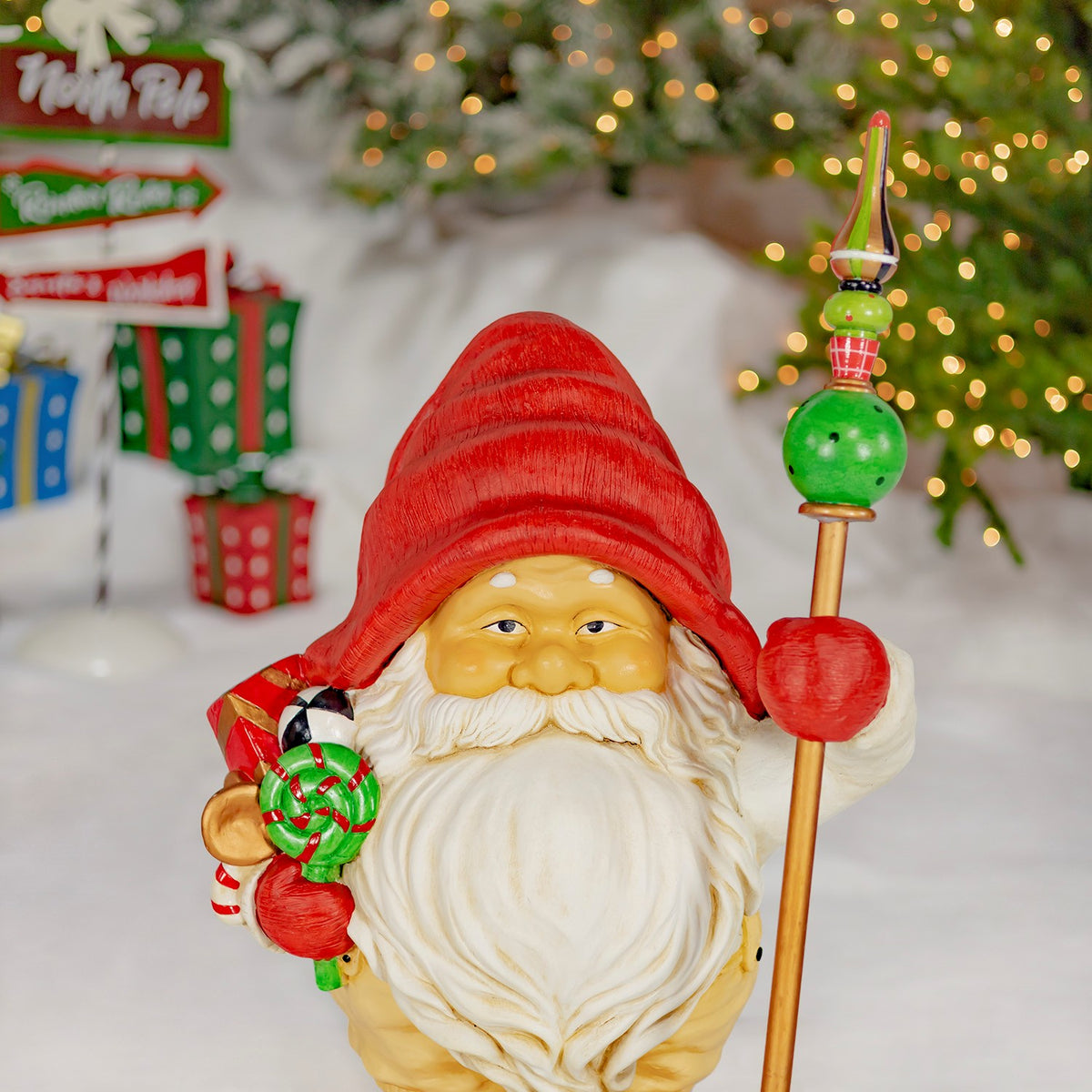 Santa gnome with a red hat holds a decorated staff and a bundle of colorful gifts.
