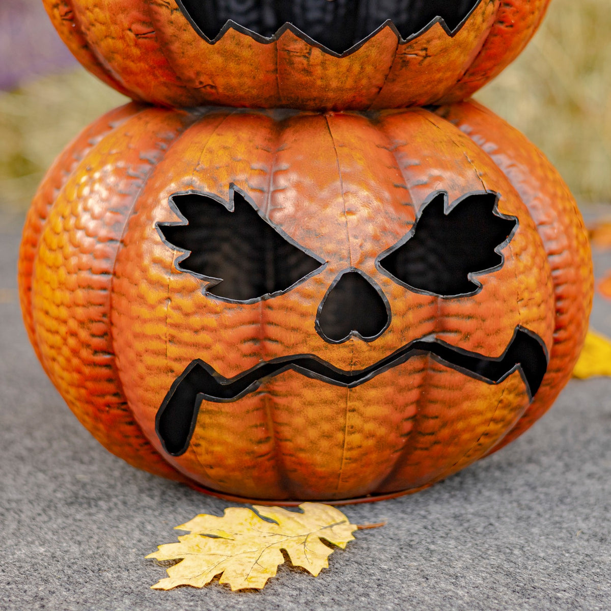 Close-up of the lower two stacked orange pumpkins, showing textured surfaces and black carved-style facial cutouts.