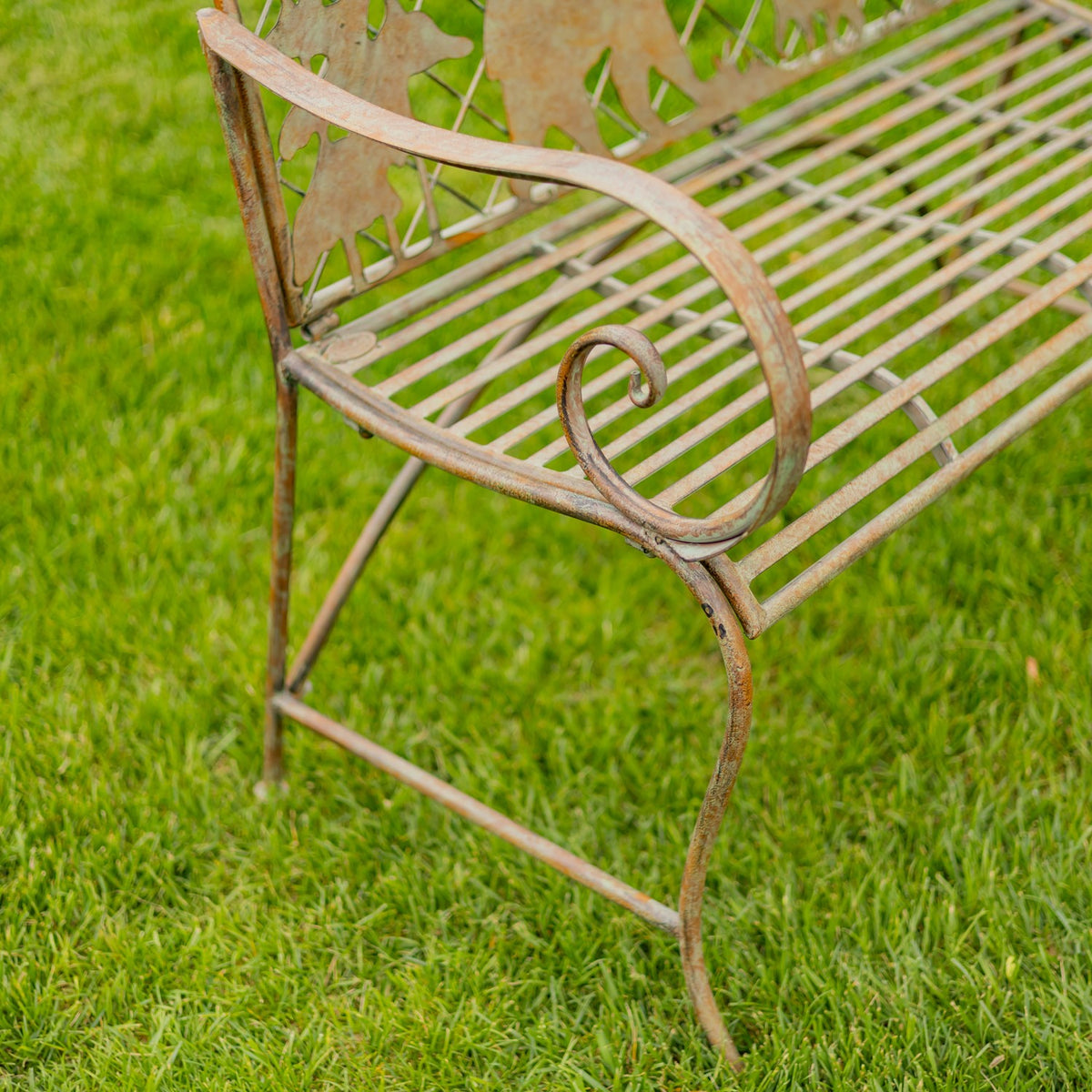 Close view of the bench’s curled metal arm, slatted seat, and decorative back on a lawn.