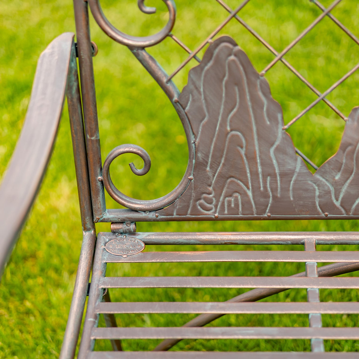 Close-up of the bench’s iron seat slats, curled side scrollwork, and raised mountain shapes on the back.
