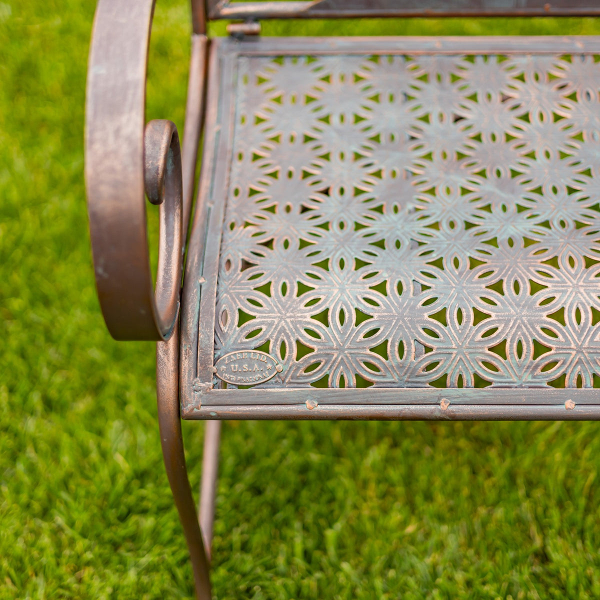 Close-up of the bench’s patterned metal seat, curved arm, and front edge outdoors.
