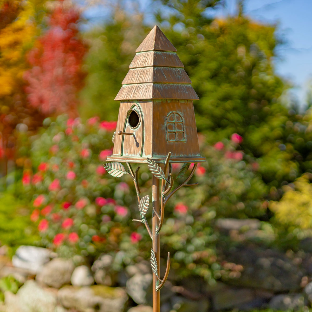 Angled view of the copper birdhouse and leafy iron stake among garden flowers