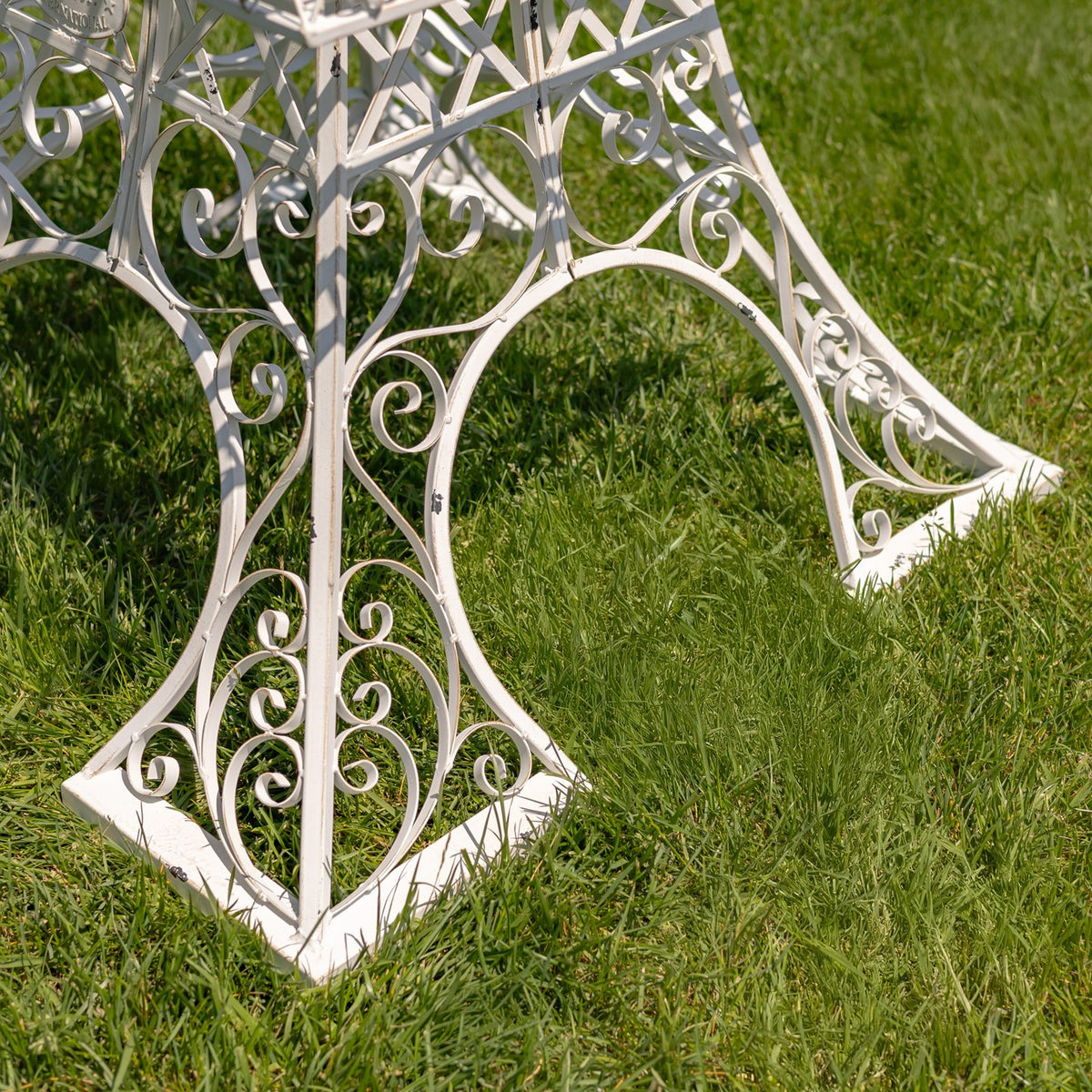 Close view of the stand’s flared feet and curled ironwork resting on grass.